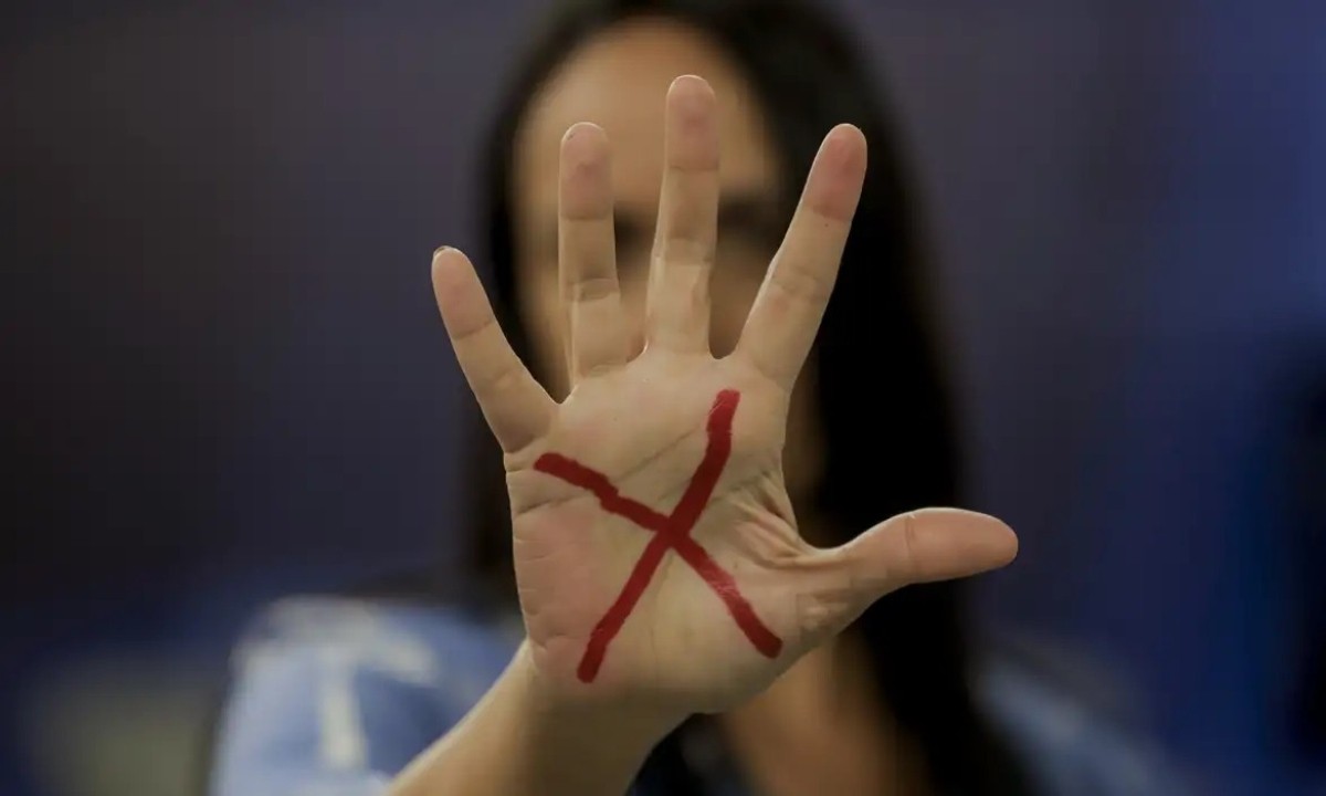mulher com um x vermelho desenhado nas maos